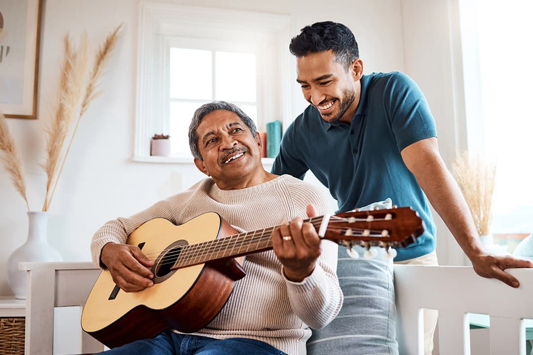 An older man playing guitar with his son beside him